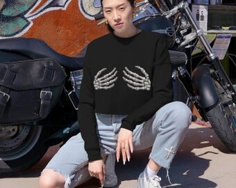 May include: A black cropped sweatshirt with a skeleton hand graphic on the front. The sweatshirt is worn by a person sitting on a motorcycle.