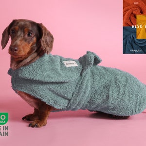 May include: A dachshund wearing a teal dog robe. The robe is made of a soft, absorbent material and has a wrap-around design. The image also shows color swatches of the robe in rust, deep pink, gold, vintage blue, and mint. The robe is eco-friendly and made in Britain.