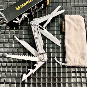 May include: A multi-tool with various implements, including scissors, a saw, and a bottle opener, is displayed open. The tool is silver and has a black box with the word "TRAVELER" and a logo. A beige pouch with the "TRAVELER" logo is also included.