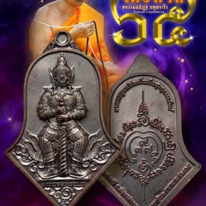 May include: Two antique Thai amulets with detailed relief carvings. One features a guardian figure, the other intricate patterns. The background includes a monk and gold lettering. The amulets are approximately 1.6 inches tall.