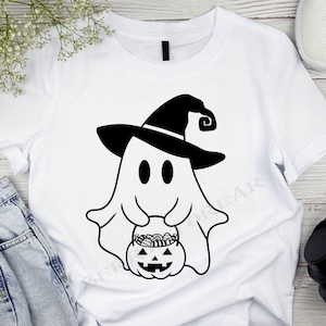 May include: White t-shirt with a black and white illustration of a ghost wearing a witch hat and holding a pumpkin filled with candy.