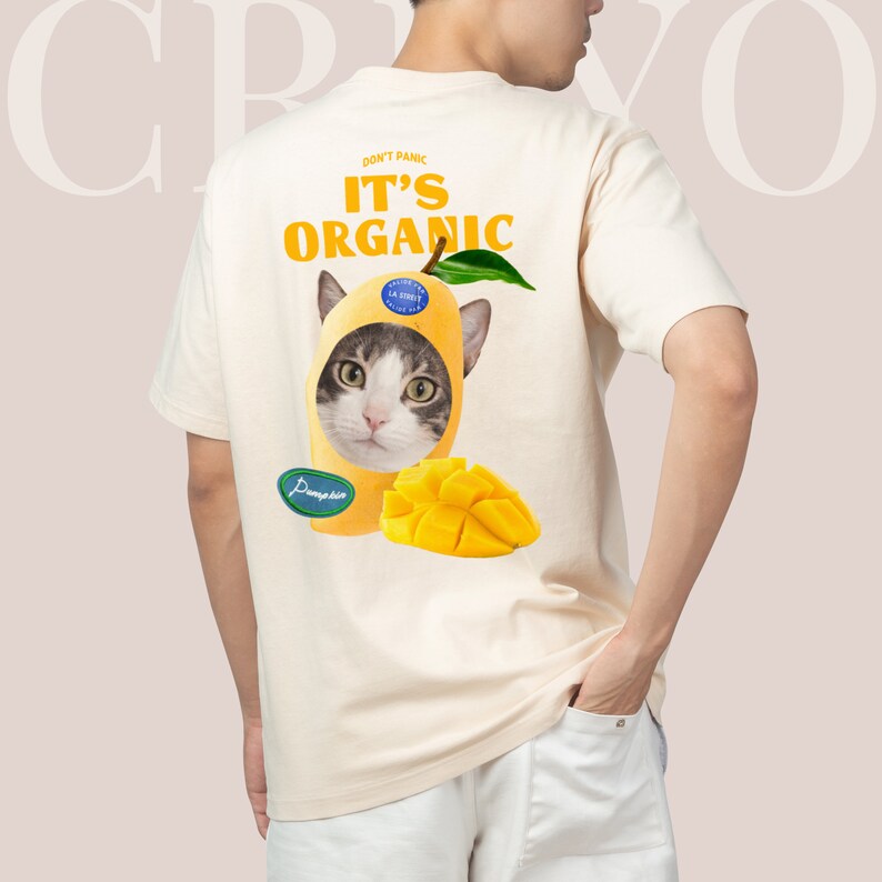 May include: A cream-colored t-shirt with a cat wearing a mango on its head. The shirt has the text "Don't Panic It's Organic" printed on it.