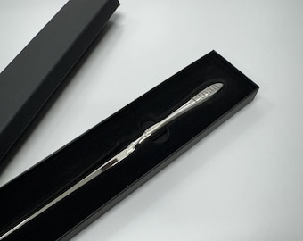May include: A silver letter opener with a black box. The letter opener has a decorative handle and a sharp point.