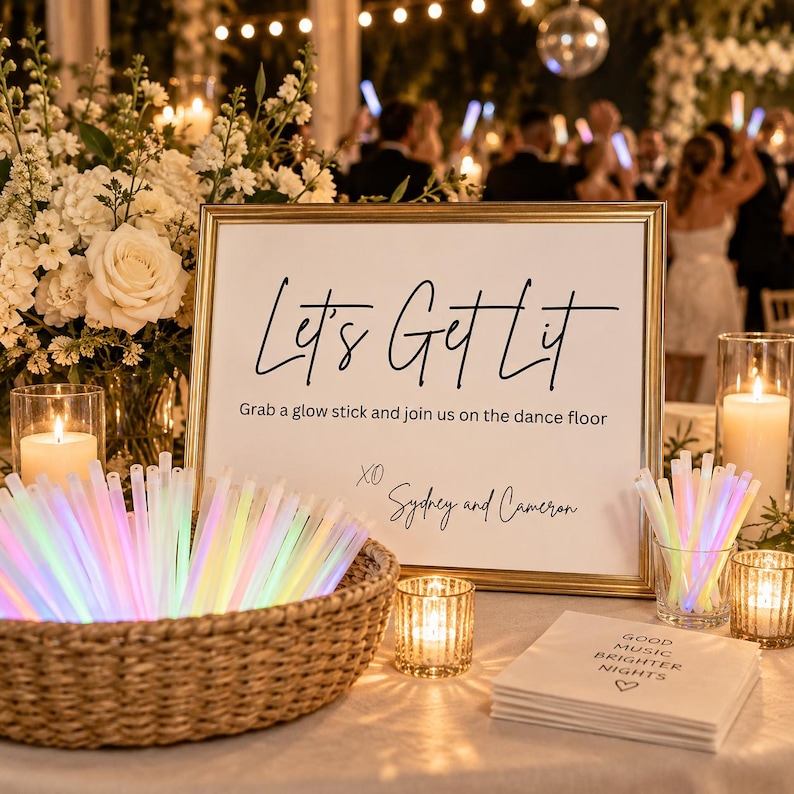 May include: A gold-framed sign with black text reading Let's Get Lit, Grab a glow stick and join us on the dance floor, XO Sydney and Cameron. A woven basket holds glowing multi-colored light sticks, alongside white napkins with printed text.