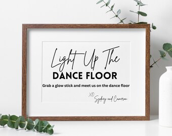 May include: A white framed sign with black text that reads "Light Up The Dance Floor" and "Grab a glow stick and meet us on the dance floor XO Sydney and Cameron".