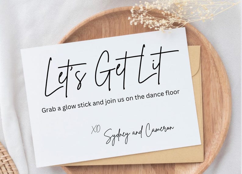 May include: A white card with black text that reads 'Let's Get Lit' and 'Grab a glow stick and join us on the dance floor.' Below the text is 'XO Sydney and Cameron'.