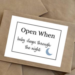 May include: A brown envelope with a white card that reads "Open When baby sleeps through the night" in black text. A blue crescent moon graphic is on the bottom right corner of the card.
