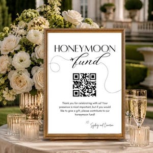 May include: A rectangular gold-framed sign with white background and black text reading HONEYMOON fund, featuring a small airplane icon, a QR code, and the text Thank you for celebrating with us! Your presence is most important, but if you would like to give a gift, please contribute to our honeymoon fund! XO Sydney and Cameron.
