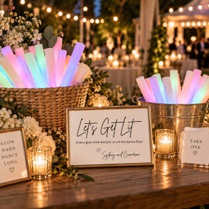 May include: A collection of glowing LED foam sticks in a woven basket and a metal bucket, accompanied by three framed signs. The central sign reads Let's Get Lit, Grab a glow stick and join us on the dance floor, XO Sydney and Cameron.