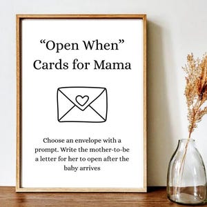 May include: A framed print with the text "Open When" Cards for Mama, featuring an envelope graphic with a heart. The print is displayed with a vase of dried flowers.