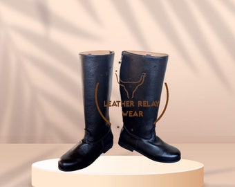 May include: A pair of black leather riding boots with a zipper on the inside of each boot. The boots are on a white pedestal against a light brown background.