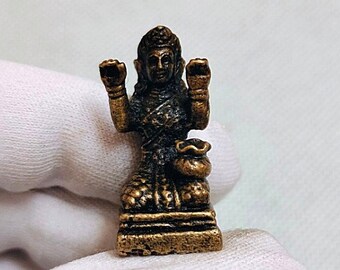 May include: A small, gold-colored statue of a deity with four arms, holding a bag of money in one hand. The statue is sitting on a base with intricate details.