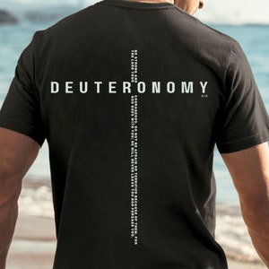 Puede incluir: Camiseta negra con texto blanco que dice "DEUTERONOMY 31:6" y una línea de texto vertical que dice "BE STRONG AND THE LORD YOUR COURAGEOUS. DO NOT BE AFRAID OR TERRIFIED BECAUSE OF THEM, FOR GOD GOES WITH YOU; HE WILL NEVER LEAVE YOU NOR FORSAKE YOU."