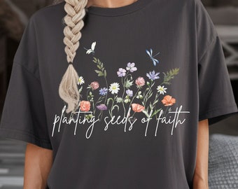 May include: A dark gray t-shirt with a floral design and the text "planting seeds of faith" in white.