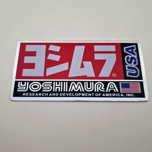 May include: A red and white sticker with the text "ヨシムラ" in Japanese characters and "YOSHIMURA" in English. The sticker also includes the text "USA" and "RESEARCH AND DEVELOPMENT OF AMERICA, INC."