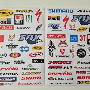 Peut inclure: Deux feuilles blanches présentant une collection d'autocollants et de logos de marques de vélos colorés. Les autocollants incluent des noms tels que Shimano, Fox, Mavic, Rock Shox, DT Swiss, Cervélo, Easton, Michelin, S-Works, Trek et Colnago, ainsi que divers icônes graphiques.