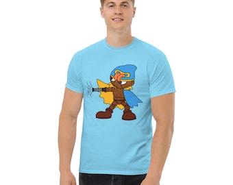 Op de afbeelding: Een lichtblauw t-shirt met een cartoonfiguur dat een blauw en geel kostuum draagt. Het personage houdt een wapen vast en heeft een vastberaden uitdrukking.