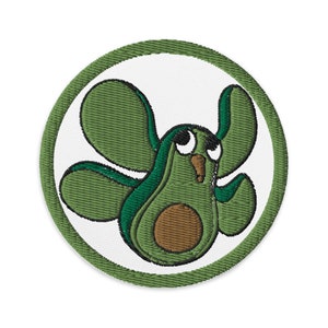 Puede incluir: Parche bordado con un aguacate de dibujos animados con alas, un hueso marrón y ojos grandes. El aguacate es verde con detalles verde oscuro, sobre un fondo blanco y enmarcado por un borde verde cosido.