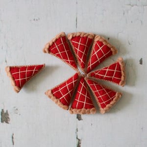 May include: Eight felt pie slices in red and brown arranged in a circle on a white wooden background.