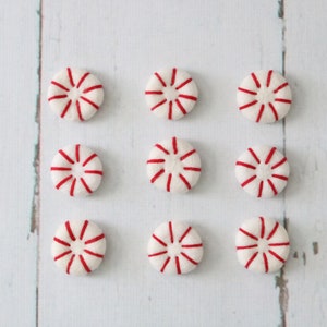 May include: Nine white peppermint candies with red stripes arranged in three rows of three on a white wooden surface.