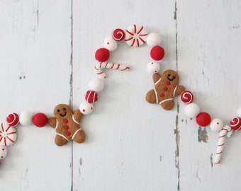 May include: A festive garland with red and white felt balls, gingerbread men, candy canes, and peppermint candies.