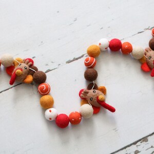 May include: A felt garland with orange, brown, white, and red balls and three felt turkey decorations. The garland is strung together with white thread.