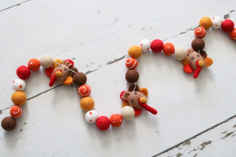 May include: A felt garland with orange, brown, white, and red balls and three felt turkey decorations. The garland is strung together with white thread.