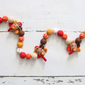 May include: A garland of felt balls in orange, red, white, and brown with three felt turkey decorations. The garland is strung on a white string and is perfect for Thanksgiving decor.