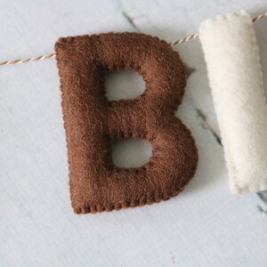 May include: Brown felt letter "B" with white stitching, part of a felt banner.