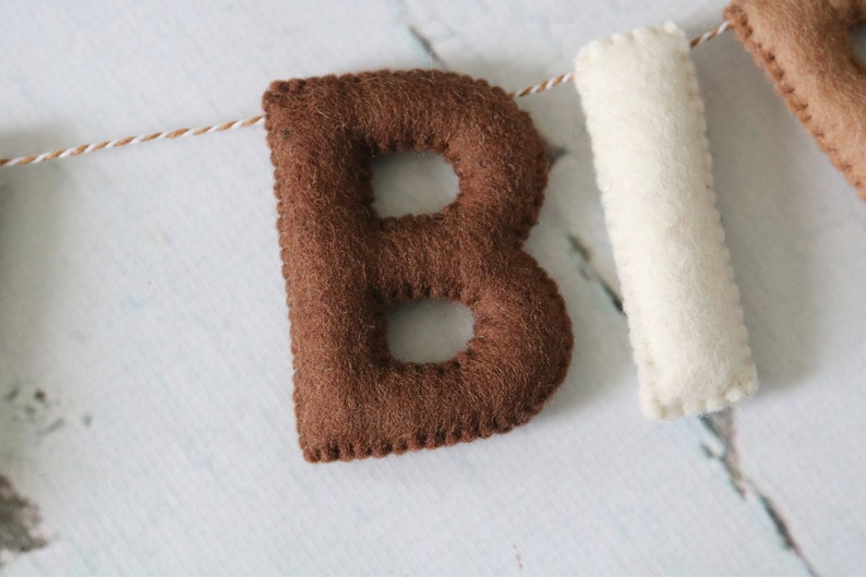 May include: Brown felt letter "B" with white stitching, part of a felt banner.