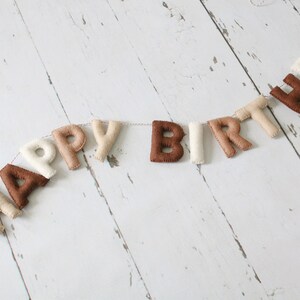 May include: A felt banner with the words "Happy Birthday" in brown, beige, and white letters.