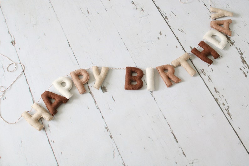 May include: A felt banner with the words "Happy Birthday" in brown, beige, and white letters.
