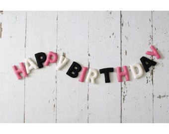May include: A felt banner with the words "Happy Birthday" in black letters with pink and white accents.