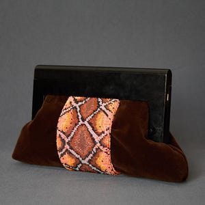 Peut inclure: Une pochette en velours marron avec une bande à motif peau de serpent perlée. La pochette a un cadre noir et une forme douce et arrondie. La bande perlée présente des nuances d'orange, de rose et de marron.