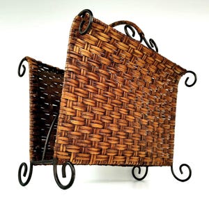 May include: A woven rattan magazine rack with a dark brown finish. The rack has a rectangular shape with a curved top and is supported by a black metal frame with decorative scrollwork. The rack is designed to hold magazines and other reading materials.
