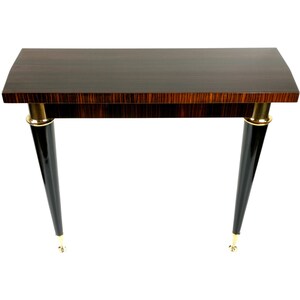 以下が含まれることがあります： 暗い縞模様の木製天板の小さな長方形テーブル。 テーブルには、上部と下部に金色のアクセントが付いた、黒色の先細りの脚が4本あります。 テーブルはスタイリッシュな家具です。