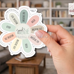 Könnte beinhalten: Ein blütenförmiger Aufkleber mit den Worten "just BREATHE" in der Mitte. Der Aufkleber hat pastellfarbene Blütenblätter mit den Anweisungen: "Breathe In", "Hold" und "Breathe Out". Der Aufkleber wird in einer Hand gehalten.