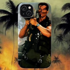 May include: A phone case featuring a movie scene with a man holding a weapon. The image has a tropical background with palm trees and a fiery sky. The man is wearing a military vest and pants, and a watch. The phone case is designed for an iPhone.