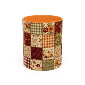 May include: A cylindrical ceramic mug featuring a patchwork design of various autumn-themed patterns including green and white gingham, orange plaid, floral prints, dark red polka dots, and illustrations of pumpkins, with a solid orange interior.