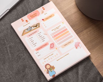 May include: A pink Ramadan Planner notepad with a cartoon illustration of a woman holding flowers. The notepad includes sections for daily goals, gratitude, and a hydration tracker. The notepad is on a wooden desk.