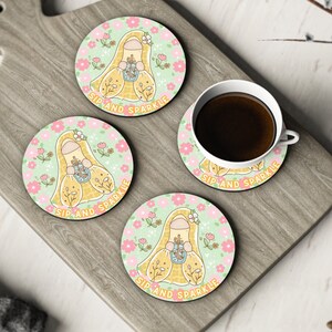 May include: Four round coasters with a green background and pink flowers. Each coaster features a cartoon illustration of a person wearing a yellow dress and holding a cup. The text "Sip and Sparkle" is printed on each coaster.