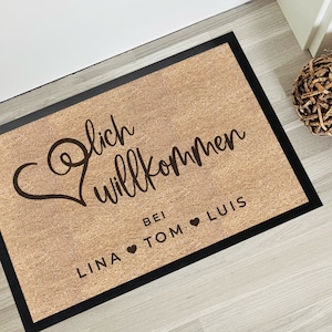 Könnte beinhalten: Eine braune Fußmatte mit schwarzem Rand und dem Text "Herzlich willkommen bei Lina Tom Luis" mit einem Herzsymbol zwischen jedem Namen.