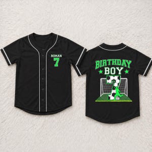 May include: Black baseball jersey with white trim and buttons. The front features the name "ROMAN" and the number "7" in green. The back displays "BIRTHDAY BOY" in green with a soccer-themed graphic.