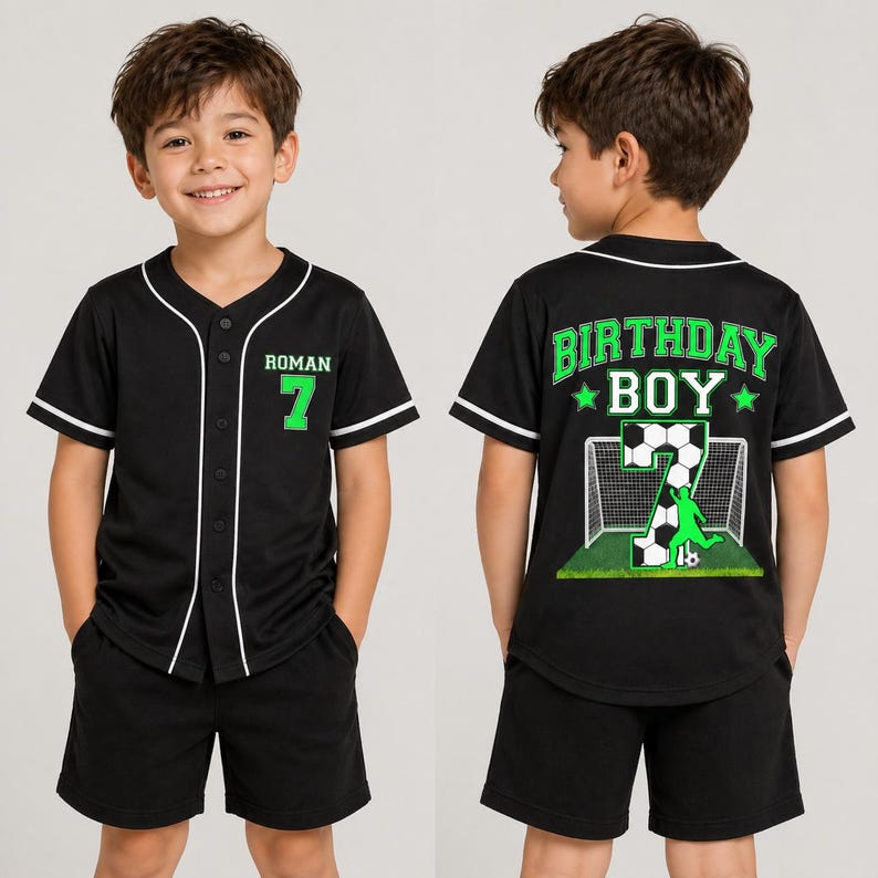May include: Black baseball-style jersey and shorts set. The jersey has white trim, the name "ROMAN" and the number "7" in green. The back of the jersey says "BIRTHDAY BOY" with a soccer-themed graphic. The shorts are black.