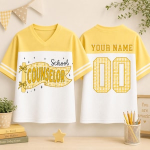 May include: A yellow and white V-neck jersey featuring a yellow banner graphic with the text School COUNSELOR on the front and the text YOUR NAME above the number 00 on the back. The shirt has short sleeves with two white stripes on each arm.