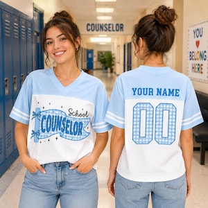 May include: A light blue and white V-neck jersey with short sleeves and white stripes. The front features a blue banner with the text School COUNSELOR and star accents. The back displays the text YOUR NAME above the number 00 in blue gingham print.