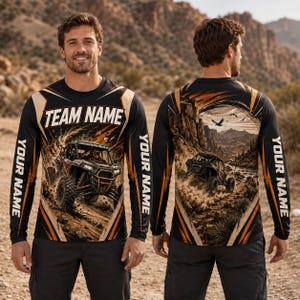 Op de afbeelding: Een shirt met lange mouwen met een zwart-oranje afbeelding van een terreinwagen in een woestijnlandschap. De voorkant toont de tekst TEAM NAME en YOUR NAME, terwijl de achterkant een gedetailleerde woestijnscène met een voertuig toont.