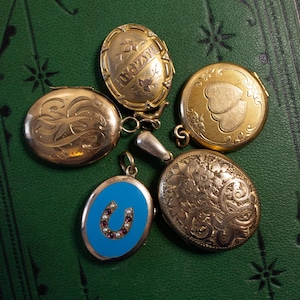 May include: Five antique gold locket pendants with intricate designs. One locket has a blue enamel background with a horseshoe design and red gemstones. Another locket has a heart design with a floral pattern. The other three lockets have engraved floral patterns.