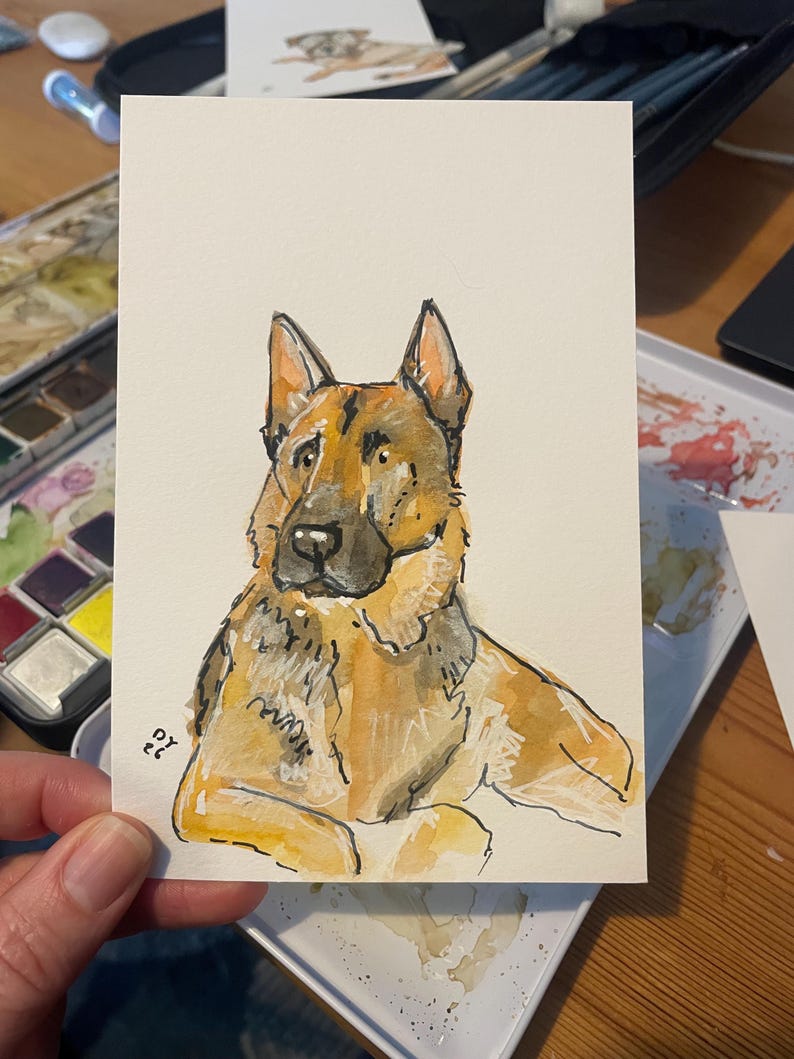 Puede incluir: Pintura a la acuarela de un perro pastor alem&aacute;n. El perro est&aacute; representado en tonos marrones, beige y negro, con un contorno detallado. La obra de arte est&aacute; sobre una tarjeta rectangular blanca, con las iniciales del artista en la esquina inferior izquierda.