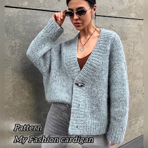 Può includere: Un cardigan blu chiaro con scollo a V e un solo bottone di chiusura. Il cardigan è realizzato in un materiale morbido e soffice e ha una vestibilità rilassata. La modella indossa il cardigan con una canotta marrone e jeans grigi. Il testo "Pattern My Fashion cardigan" è visibile nella parte inferiore dell'immagine.
